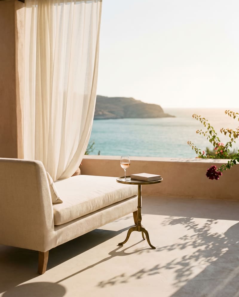 A cream linen chaise longue on a sun-warmed boutique-hotel terrace overlooking a calm Mediterranean bay at golden hour.
