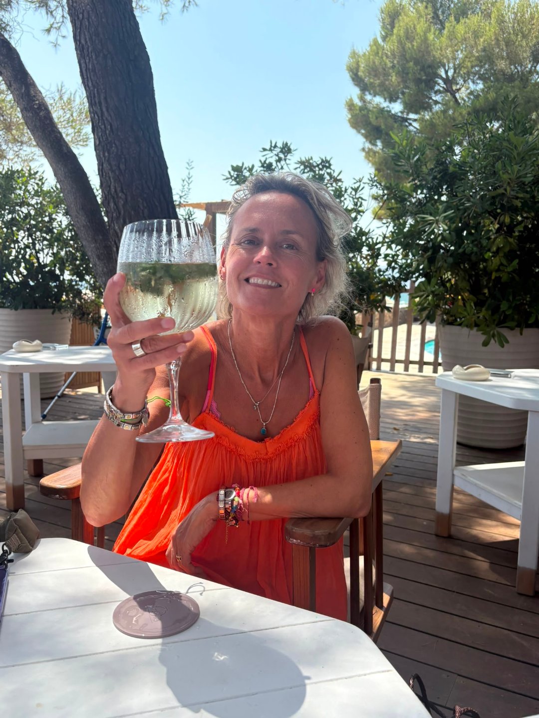 Lulu Townsend smiling on a sunlit terrace in a pink blouse, green hills soft in the distance.