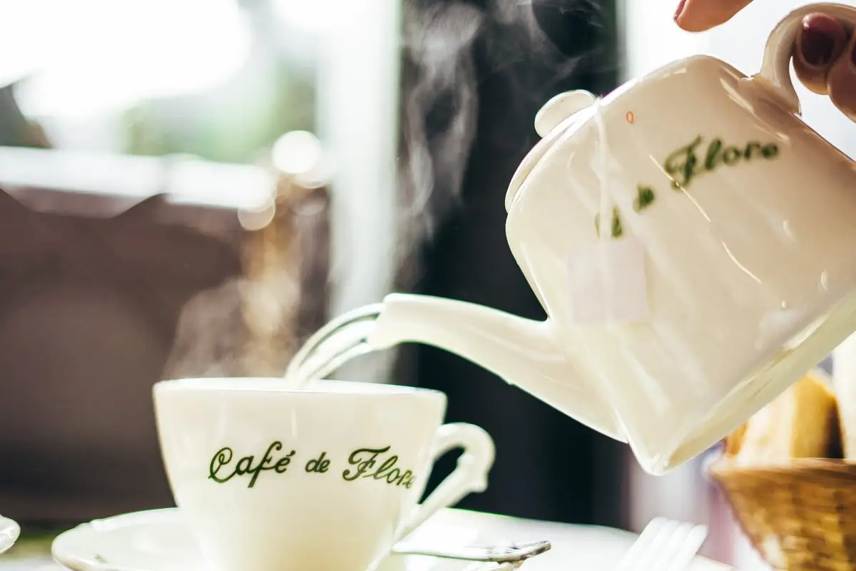 Teapot pouring hot tea into a Café de Flore cup at a Parisian café table.