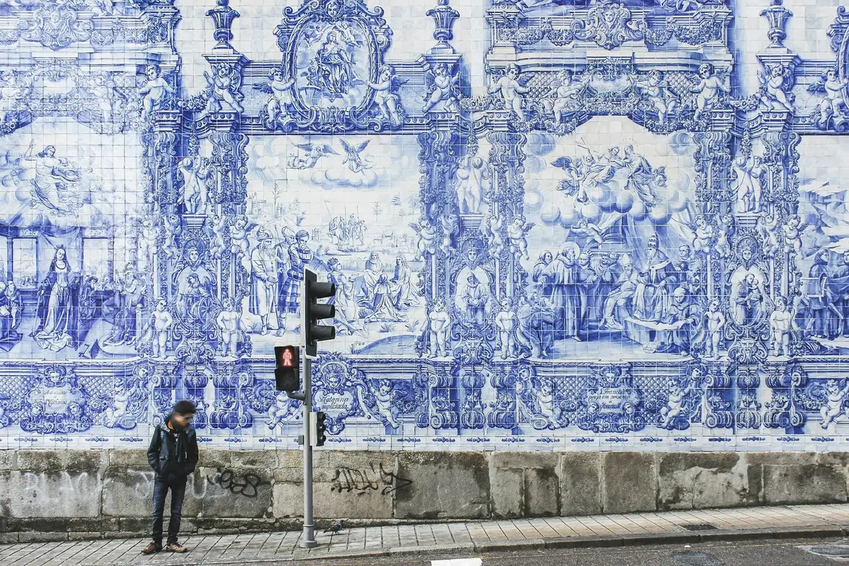 Man standing by a traffic light in front of ornate blue-and-white tiled mural in Portugal.