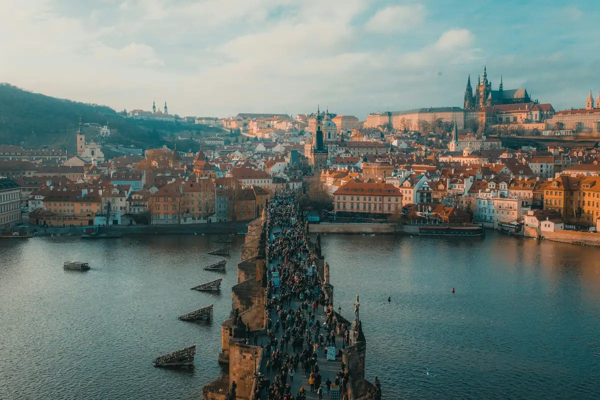 Aerial view of Charles Bridge in Prague with crowds overlooking the Vltava River and city skyline.