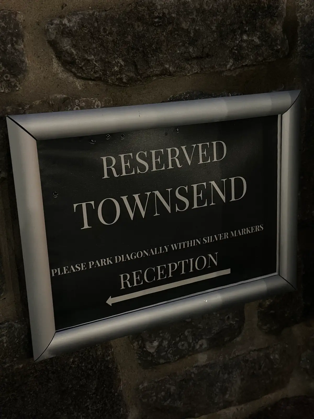 eserved parking sign for Townsend outside a stone wall, with arrow to reception.